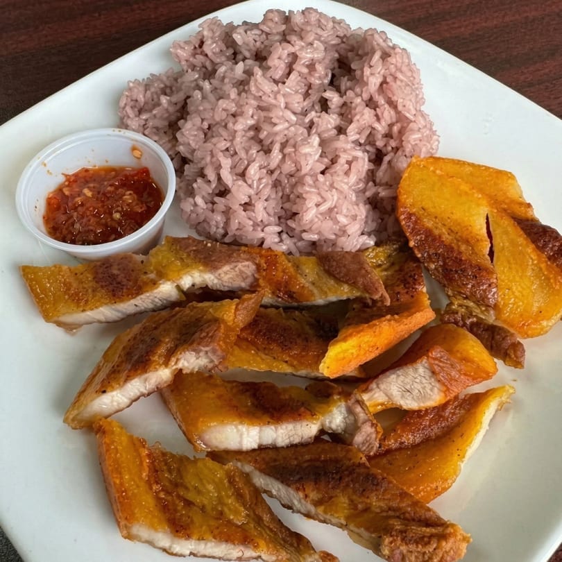 Crispy pork belly slices with purple rice and a side of chili sauce on a white plate.