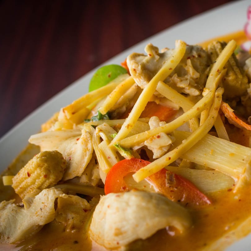 Close-up of a Thai curry dish with chicken, bamboo shoots, baby corn, and red bell peppers.