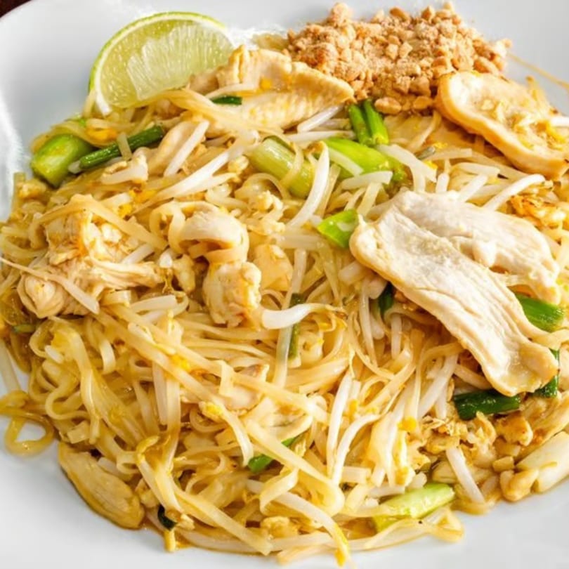 Chicken Pad Thai with noodles, bean sprouts, green onions, crushed peanuts, and a lime wedge.