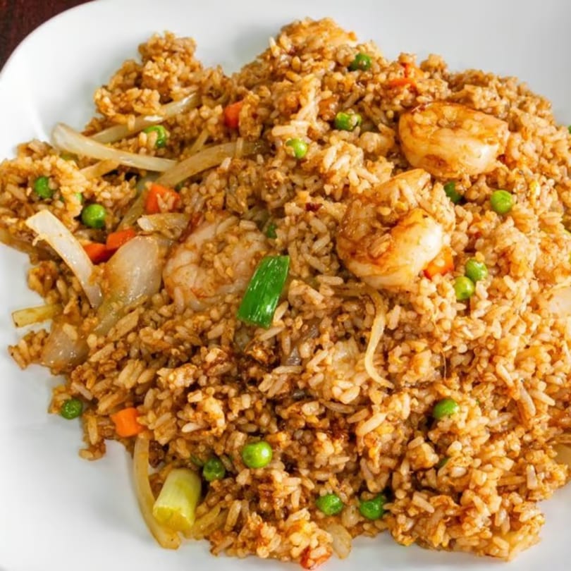 Close-up of shrimp fried rice with peas, carrots, and onions on a white plate.